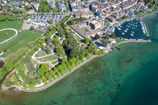Aerial view of Chateau de Morges, the marina with sailboats, and the lush Parc de l'Independance along the shores of Lake Geneva in Morges, Vaud, Switzerland.