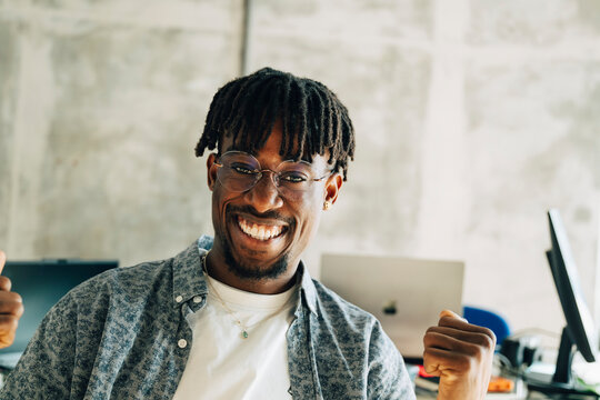 Portrait of of cheerful businessman holding fists while celebrating success at modern office
