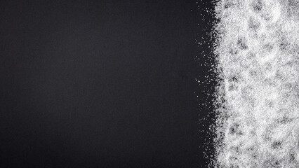 Top view of spilled sugar scattered across deep black background, creating striking contrast and minimalist composition. Large empty copy space for product placement or advertising text.  © magdal3na