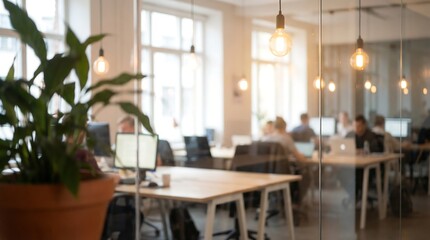 Fototapeta premium Open plan office interior with warm hanging pendant lights over wooden desks and lush green plants through glass partition in creative and modern professional coworking environment