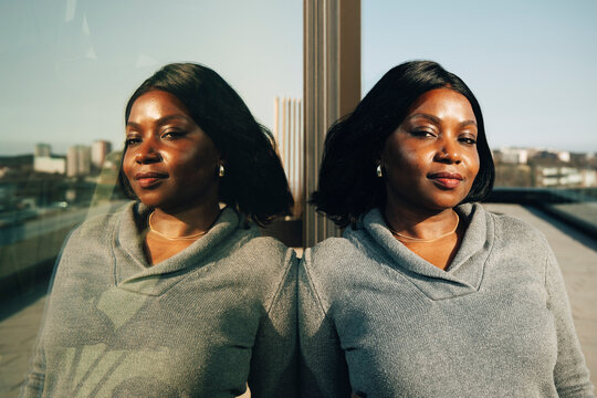 Portrait of confident businesswoman leaning on glass wall in office balcony