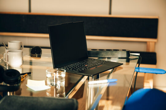 Black laptop with blank screen on glass desk in modern office