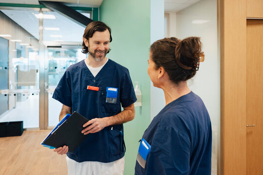 Smiling male healthcare worker talking with female coworker while standing in hospital lobby