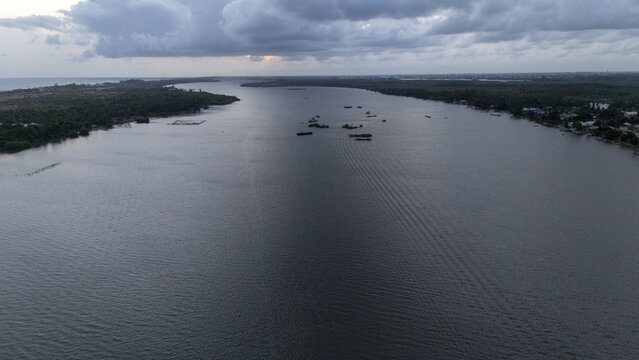 Aerial view of the wide Badagry Creek with small boats scattered on the water under a dramatic cloudy sky at dusk Badagry, Lagos, Nigeria.