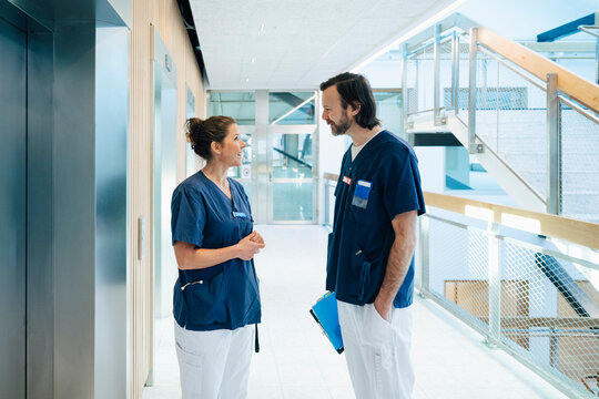 Smiling female physician talking to male nurse while standing in hospital corridor