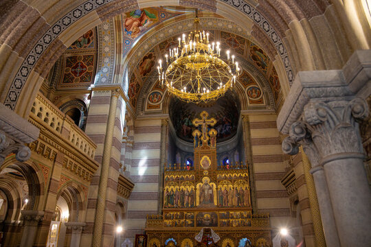 Ornate interior of an Orthodox church with a golden iconostasis and grand chandelier under stone arches.