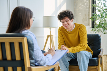 Obraz premium Happy teenage boy smiling during successful consultation with female psychologist