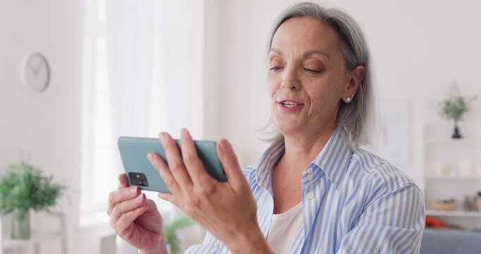 Excited happy senior retired woman, adult woman making video call on mobile phone waving getting good news on screen, smiling, talking, chatting on Internet, using online app for family communication 