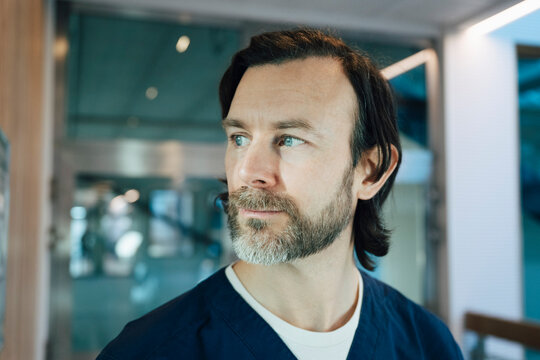Contemplative male doctor looking away while standing in hospital corridor