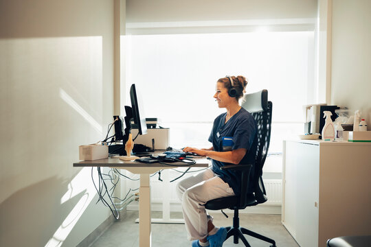 Full length of female physician wearing headset consulting through video call on computer while sitting in office at hos