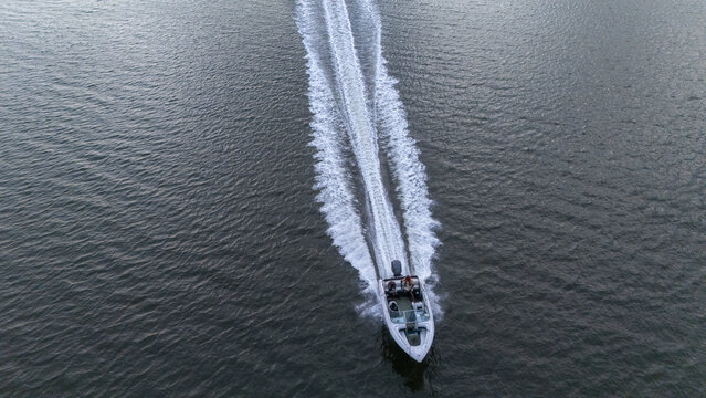 Aerial view of a motorboat cruising through dark water with people on board and a long white wake trailing behind Badagry, Lagos, Nigeria.