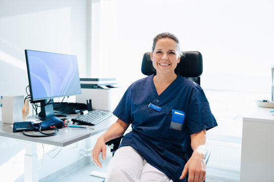 Portrait of smiling female medical professional sitting on chair near desk in office at hospital