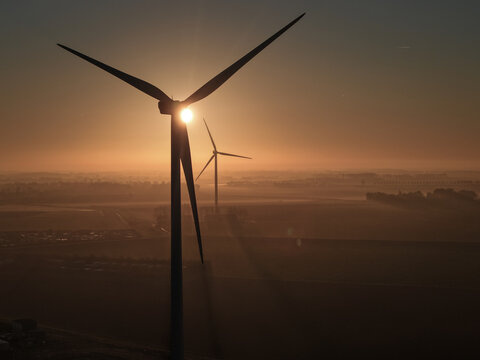 Aerial view of wind turbines silhouetted against a golden sunrise with misty fields in the background in Vrouwenpolder, Zeeland, Netherlands.