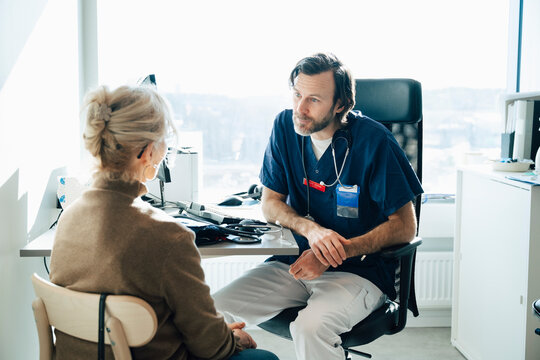 Male healthcare worker talking with female senior patient during her visit in hospital room