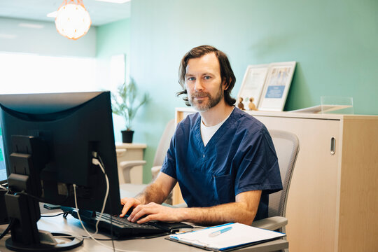 Portrait of male receptionist sitting at desk with computer in hospital