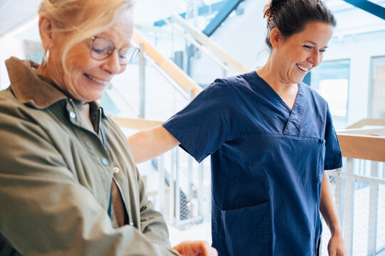 Happy female nurse walking with senior woman in hospital building