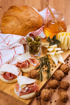 Aperitivo Italiano, tagliere con formaggio, tigelle, prosciutto crudo, miele, noci, olive e pane su tagliere