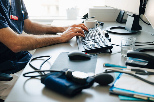 Midsection of male medical professional typing on computer keyboard while working at desk in hospital office