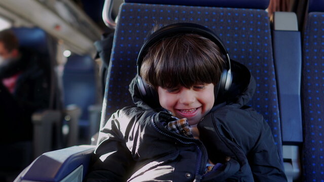 Boy listening to music with headphones on train seat, happily reacting with excitement and joy while enjoying audio entertainment during travel journey