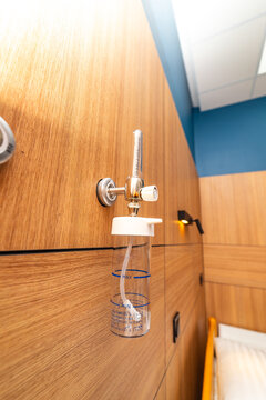 Medical oxygen flowmeter and humidifier jar on wooden wall panel. Close-up of medical oxygen regulator and humidifier bottle attached to a wooden wall in a clinic room