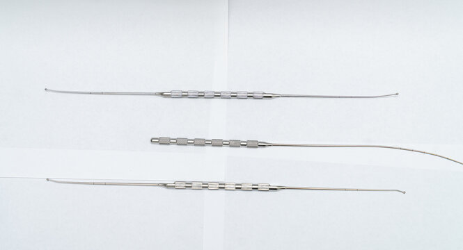 Three slender surgical probes with knurled grips on white background. Set of three thin medical instruments or nerve hooks with textured handle sections for precise surgical manipulation.