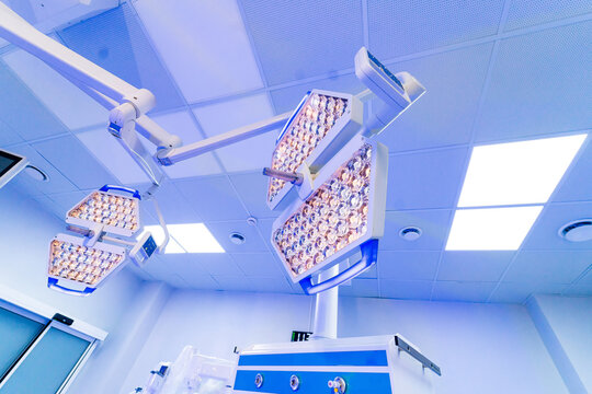 Ceiling mounted LED surgical lights in modern operating room. Bottom view of dual head surgical lamp system on ceiling in a professional medical theater with blue lighting.