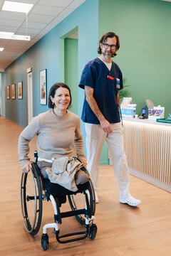 Portrait of smiling amputee woman wheeling on wheelchair near male nurse in hospital lobby