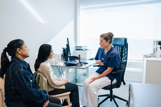 Female medical professional advising about chest problems to girl sitting with mother during visit in hospital