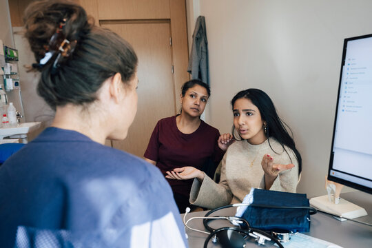 Girl explaining medical problems to female pediatrician while sitting with mother during hospital visit