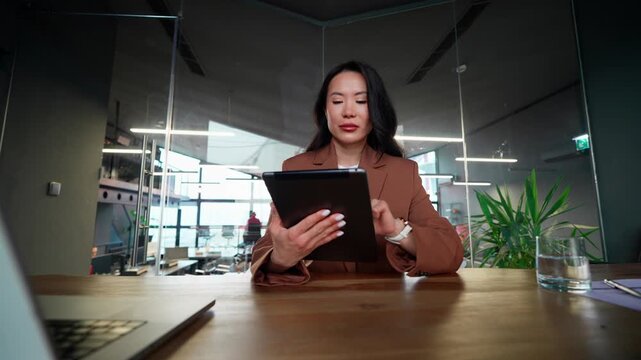 Successful smiling Asian middle-aged woman using pad computer for business. Busy executive mature CEO businesswoman professional holding digital tablet pc device for work in modern office workplace
