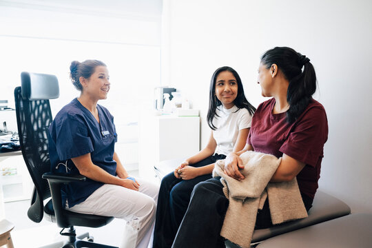 Smiling female doctor talking with mother and daughter sitting on examination table in medical clinic