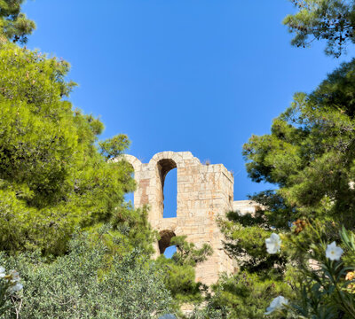 Odeon of Herodes Atticus, Herodeion stone ruins rise above green trees on the Acropolis hill in Athens, Greece.