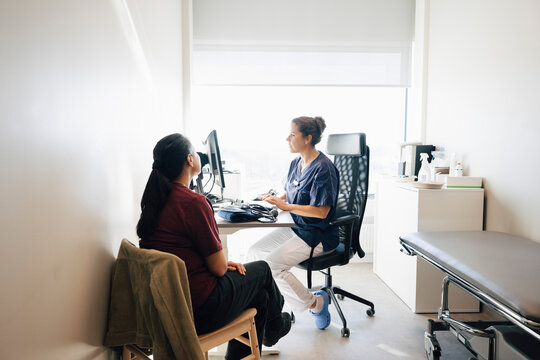 Woman sitting on chair while female doctor analyzing medical record on computer in hospital office