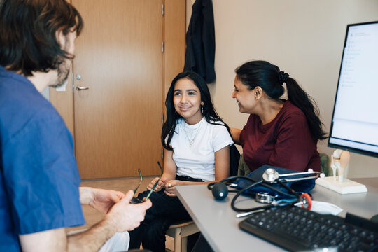 Smiling girl taking advise from male pediatrician while sitting with mother during hospital visit