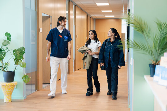 Full length of male nurse walking with mother and daughter in hospital lobby