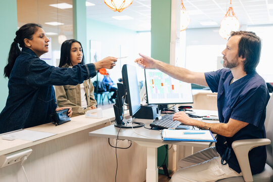 Woman giving credit card to male receptionist at desk in hospital