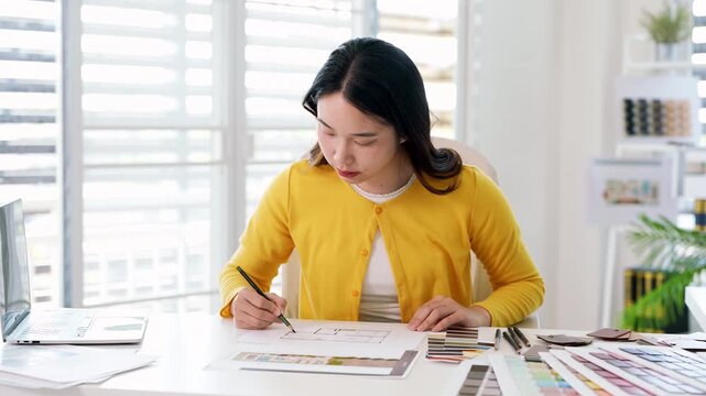 Creative female designer works on apartment design draws sketches in notebook surrounded by samples material and stationery