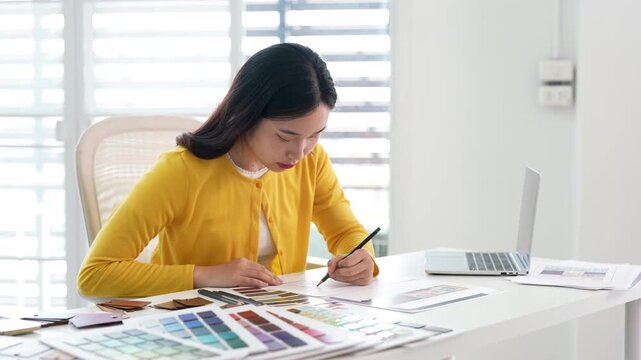 Creative female designer works on apartment design draws sketches in notebook surrounded by samples material and stationery
