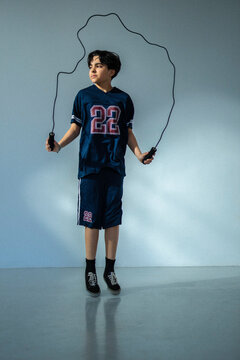 Full length of boy looking away while jumping rope against colored wall