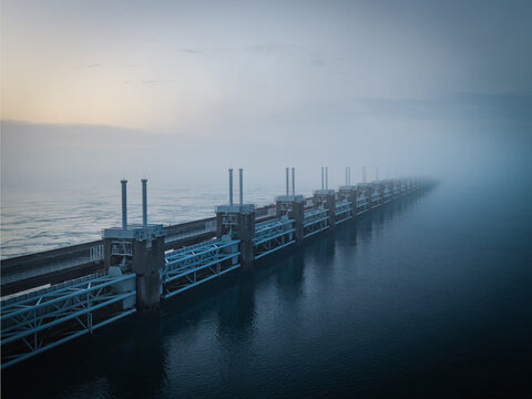 Aerial view of the Delta Projects Netherlands storm surge barrier with massive pillars and gates disappearing into thick fog over the sea in Vrouwenpolder, Zeeland, Netherlands.