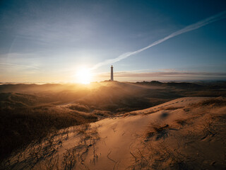 Lighthouse on sand dunes at sunrise with warm golden light, long shadows and clear sky. Ideal for coastal landscapes, travel, nature exploration and atmospheric themes. © Pavel