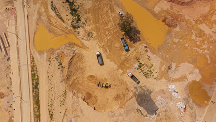 Aerial view discovering a construction site with heavy machinery including an excavator and dump trucks moving soil, creating new infrastructure and preparing the ground for future development © Nasos Zovoilis