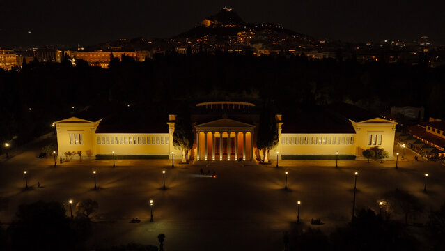 Zappeion hall illuminated at night in athens, with the acropolis and lycabettus hill glowing behind, creating a dramatic historic urban panorama of the city skyline