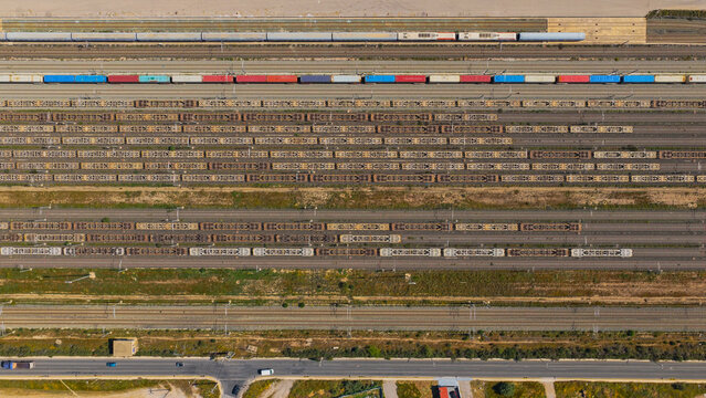 Overhead view of a busy railway yard with multiple parallel tracks and freight trains carrying colorful containers and bare wagons, showcasing large-scale logistics and transport systems