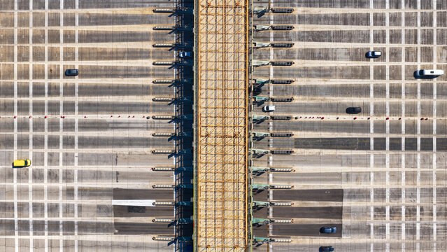 Large highway toll plaza structure with multiple lanes and a central bridge gantry, showing a few cars moving through the system or waiting on the tarmac