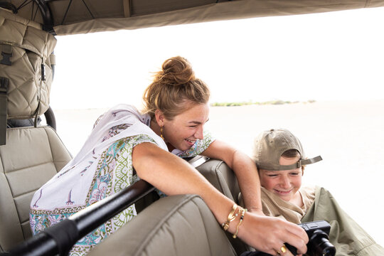 siblings reviewing images on camera in safari vehicle, Makgadikgadi Park, Botswana, Africa