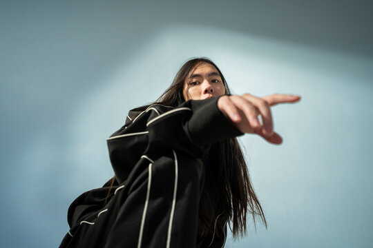 Low angle portrait of non-binary person gesturing against wall