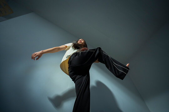Low angle view of young non-binary person practicing dance steps near wall