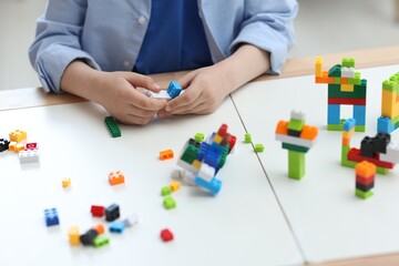 Naklejka premium Construction toy. Little boy playing with building blocks at table indoors, closeup