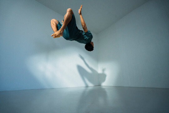 Low angle view of young male athlete doing somersault in front of wall